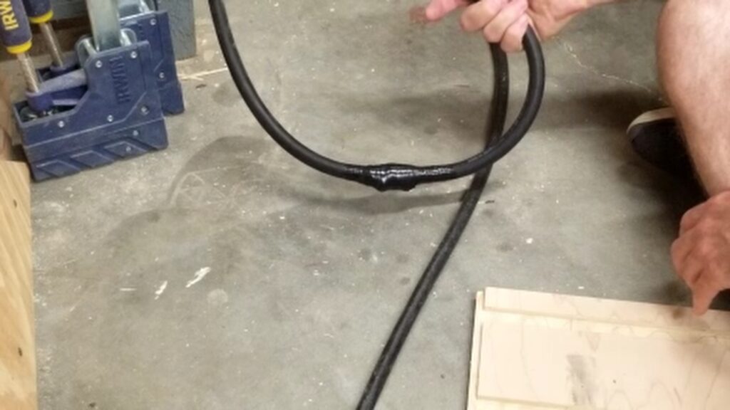A hand holding the repaired air hose showing off the black electrical tape wrapped around the hose.