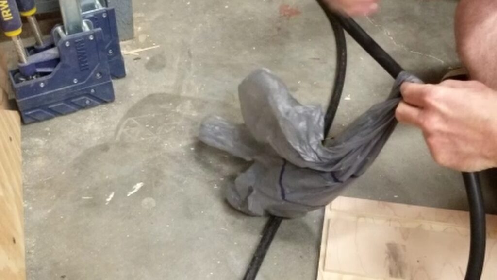 A hand wrapping a plastic grocery bag around the hose clamps that were used to repair the blowout.