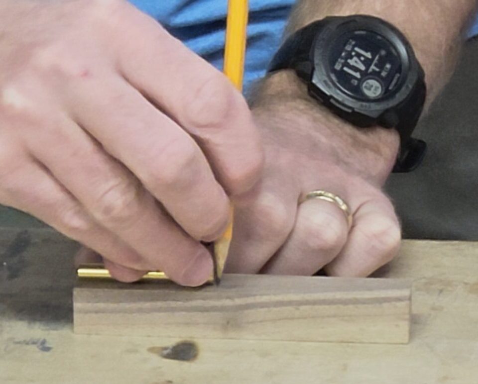 hand holding a pencil marking just slightly longer than the a brass tube on wood